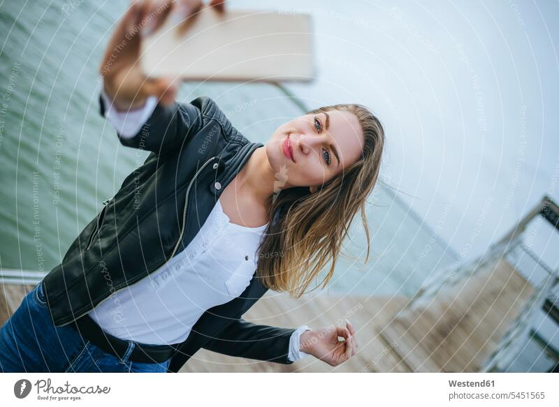 Porträt einer lächelnden jungen Frau, die ein Selfie an der Strandpromenade macht Selfies weiblich Frauen Erwachsener erwachsen Mensch Menschen Leute People