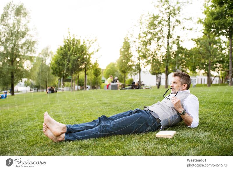 Reifer Geschäftsmann im Stadtpark auf Gras liegend liegt Wiese Wiesen entspannt entspanntheit relaxt Mann Männer männlich Pause Entspannung relaxen entspannen