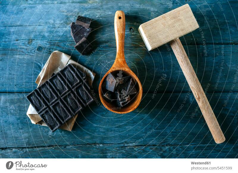 Zartbitterschokolade auf Papier, Holzlöffel und Holzhammer auf blauem Holz Papiere zerdrücken zerkleinert zerkleinern Serie Serien Bildserie Stücke Stueckchen