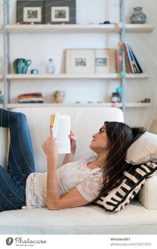 Frau liegt auf der Couch und liest ein Buch weiblich Frauen Bücher Sofa Couches Liege Sofas Erwachsener erwachsen Mensch Menschen Leute People Personen ernst