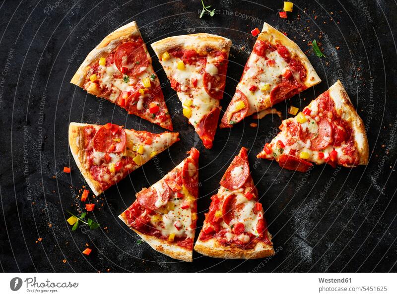 Aufgeschnittene Pizza mit Salami auf dunklem Boden Food and Drink Lebensmittel Essen und Trinken Nahrungsmittel Mozzarella Käse Kaese rote Paprika selbstgemacht