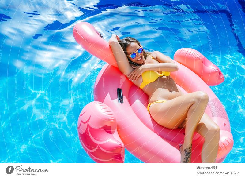 Unbeschwerte junge Frau auf rosa Flamingo schwebt im Schwimmbad glücklich Glück glücklich sein glücklichsein entspannt entspanntheit relaxt lächeln weiblich
