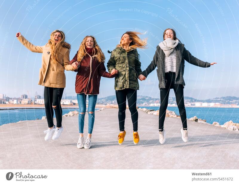 Vier Freunde halten sich an den Händen und springen in die Luft hüpfen Freundinnen Sprung Spruenge Sprünge Freundschaft Kameradschaft lachen Luftsprung