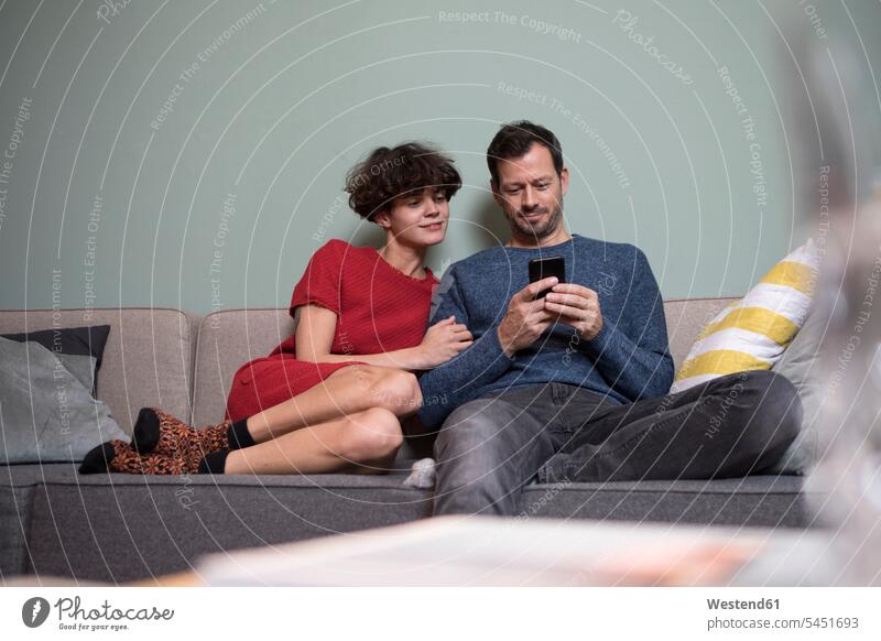 Ehepaar sitzt zusammen auf der Couch und schaut auf das Handy Sofa Couches Liege Sofas Smartphone iPhone Smartphones Paar Pärchen Paare Partnerschaft