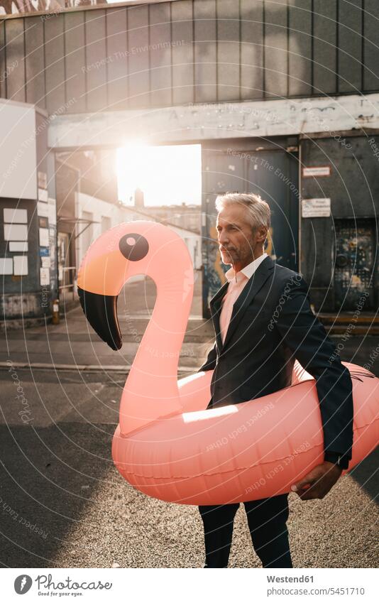 Reifer Geschäftsmann auf der Straße mit aufblasbarem Flamingo Businessmann Businessmänner Geschäftsmänner Geschäftsleute Geschäftspersonen Geschäftsleben