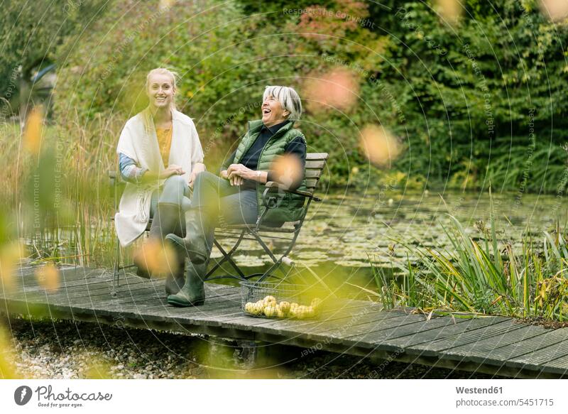 Glückliche junge Frau sitzt mit ihrer Großmutter auf dem Steg am Gartenteich Teich Teiche Grossmutter Oma Grossmama Großmütter Omi Holzsteg Holzstege Stege