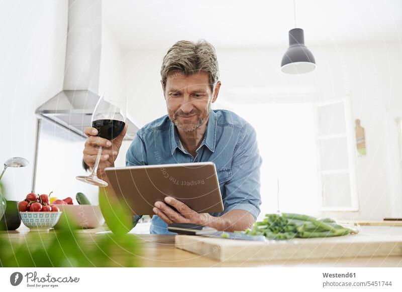 Reifer Mann in seiner Küche liest Rezept auf seinem digitalen Tablett lächeln Rotwein Rotweine Zuversicht Zuversichtlich Selbstvertrauen selbstbewusst Vertrauen
