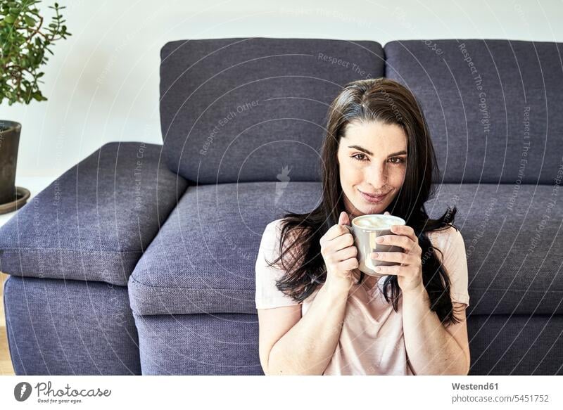 Lächelnde junge Frau mit Kaffeebecher zu Hause entspannt entspanntheit relaxt weiblich Frauen lächeln Entspannung relaxen entspannen Getränk Getraenk Getränke