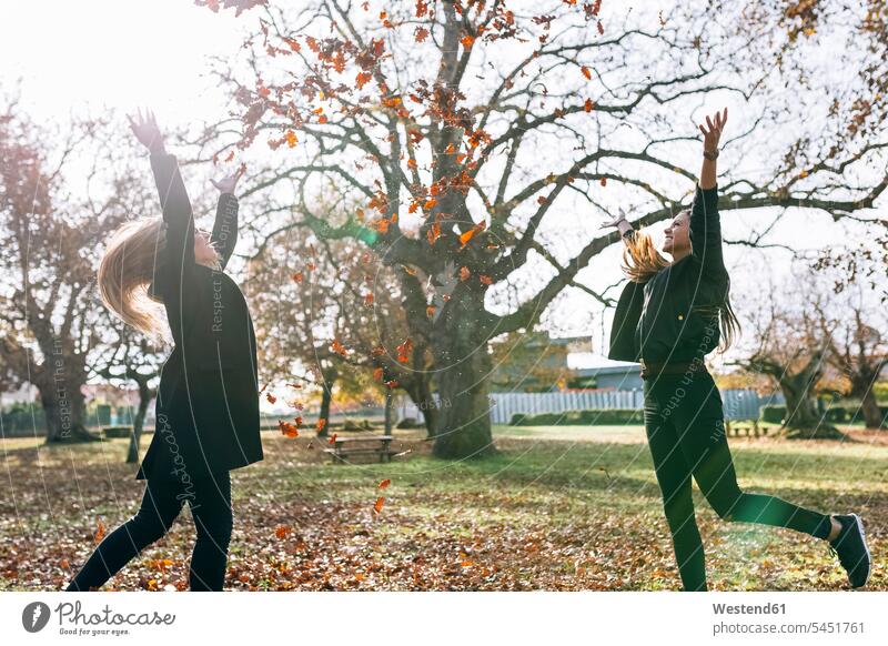 Zwei glückliche junge Frauen haben im Herbst Spaß im Park Parkanlagen Parks weiblich werfen Wurf Blatt Blaetter Blätter Freundinnen Erwachsener erwachsen Mensch
