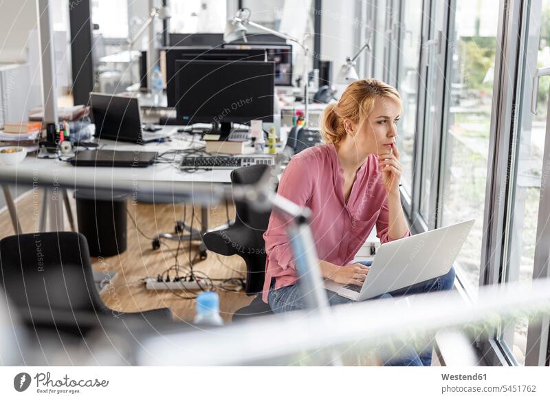 Frau mit Laptop im Büro, die aus dem Fenster schaut denken nachdenken Office Büros weiblich Frauen Notebook Laptops Notebooks Arbeitsplatz Arbeitsstätte