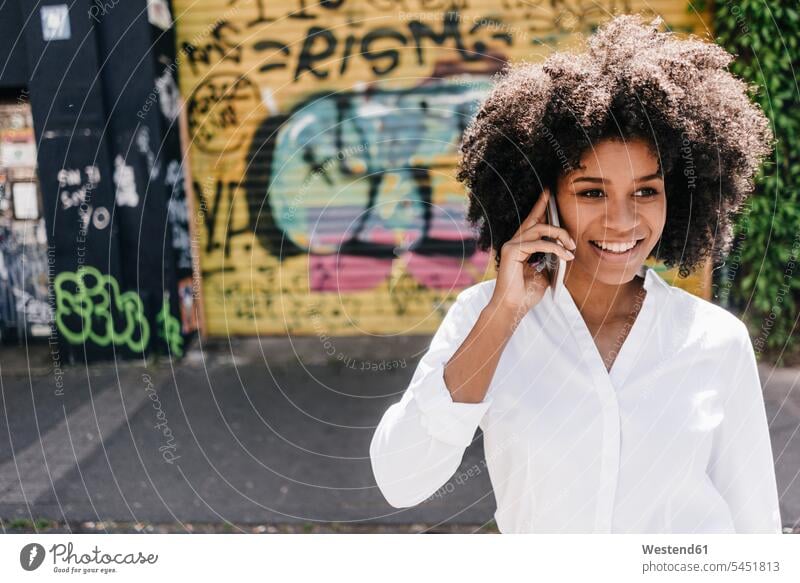 Lächelnde junge Frau am Mobiltelefon im Freien Handy Handies Handys Mobiltelefone weiblich Frauen stehen stehend steht telefonieren anrufen Anruf telephonieren