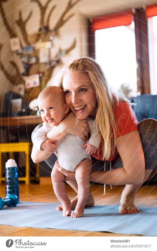 Lächelnde Mutter mit Baby und Fitnessgeräten zu Hause trainieren Mami Mutti Mütter Mama Hantel lächeln Babies Babys Säuglinge Kind Kinder Eltern Familie