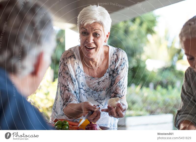 Porträt einer lächelnden älteren Frau, die mit Hilfe ihrer Freunde auf der Terrasse ein Mittagessen vorbereitet Portrait Porträts Portraits Seniorin Seniorinnen