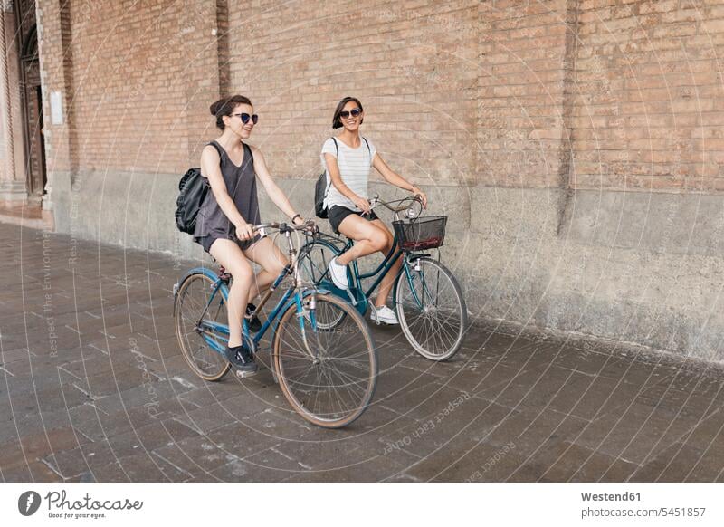 Zwei junge Frauen fahren Fahrrad in der Stadt Freundinnen radfahren fahrradfahren radeln Freunde Freundschaft Kameradschaft Bikes Fahrräder Räder Rad Raeder