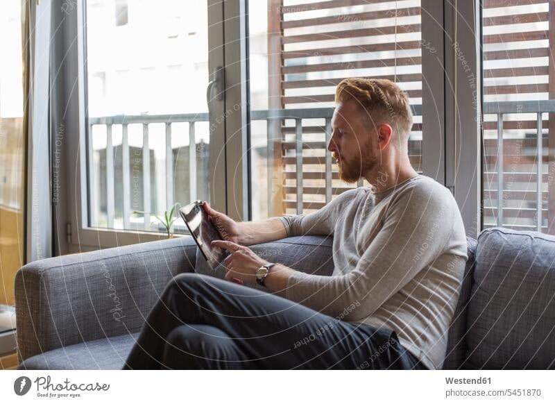 Mann benutzt Mini-Tablette auf der Couch in seinem Wohnzimmer Sofa Couches Liege Sofas Männer männlich Tablet Computer Tablet-PC Tablet PC iPad Tablet-Computer