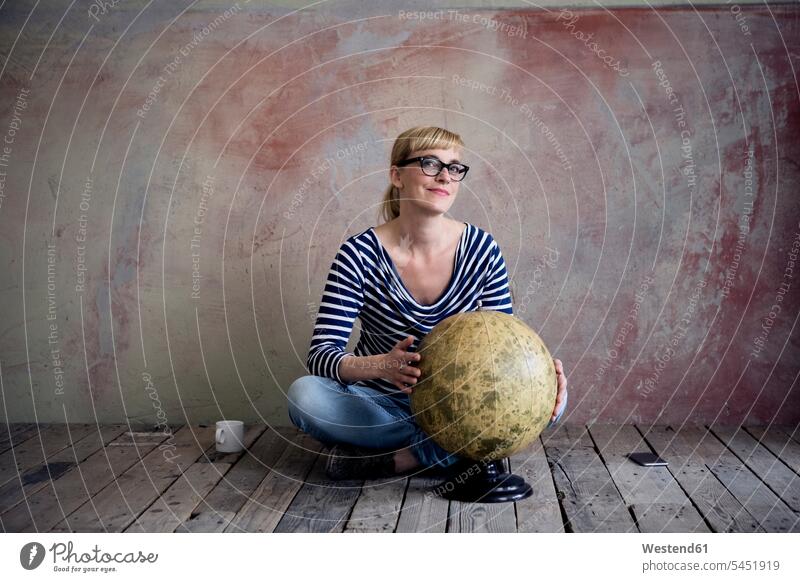 Lächelnde Frau sitzt auf einem Holzboden in einem unrenovierten Raum mit einem alten Globus weiblich Frauen Portrait Porträts Portraits Weltkugel Erdkugel
