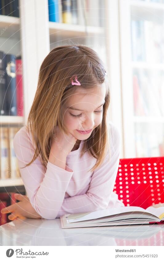 Porträt eines lächelnden kleinen Mädchens bei Tisch beim Lesen eines Buches Tische Portrait Porträts Portraits betrachten betrachtend lesen Lektüre aufstützen