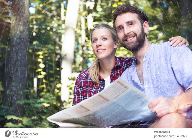 Lächelndes junges Paar mit Karte in einem Wald lächeln Pärchen Paare Partnerschaft Landkarte Landkarten Forst Wälder Mensch Menschen Leute People Personen