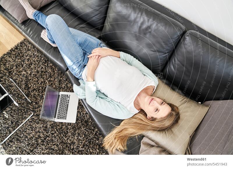 Frau liegt zu Hause auf der Couch neben dem Laptop weiblich Frauen liegen liegend Notebook Laptops Notebooks Sofa Couches Liege Sofas Erwachsener erwachsen