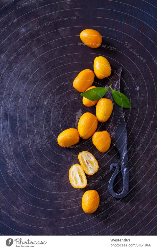 Geschnittene und ganze Kumquats, Blätter und altes Messer auf rostigem Boden Niemand Frucht Früchte Fruechte Zitrusfrucht Zitrusfruechte Zitrusfrüchte orange