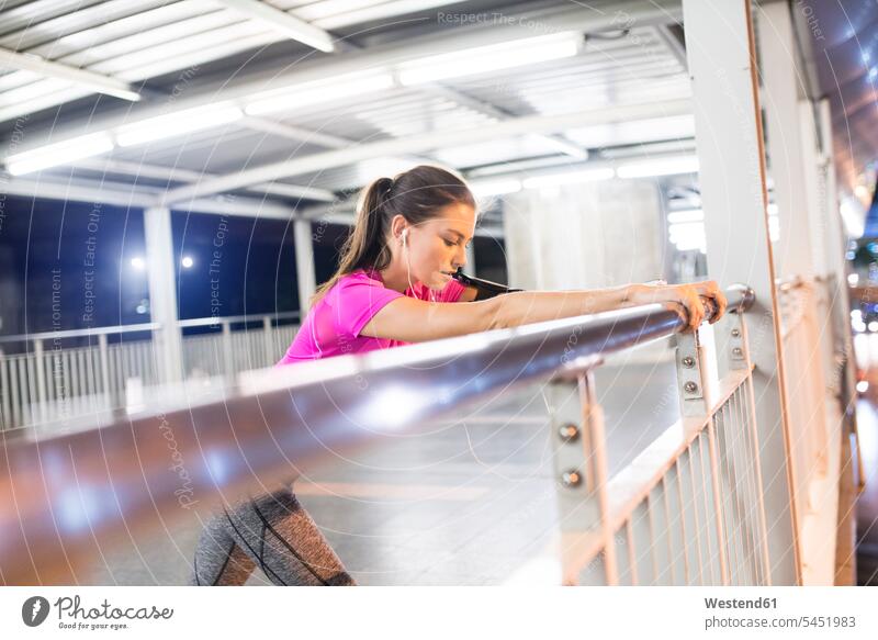 Junge Frau in rosa Sporthemd streckt sich nachts in moderner U-Bahn-Station Musik hören junge Frau junge Frauen dehnen strecken trainieren Ohrhörer Joggerin