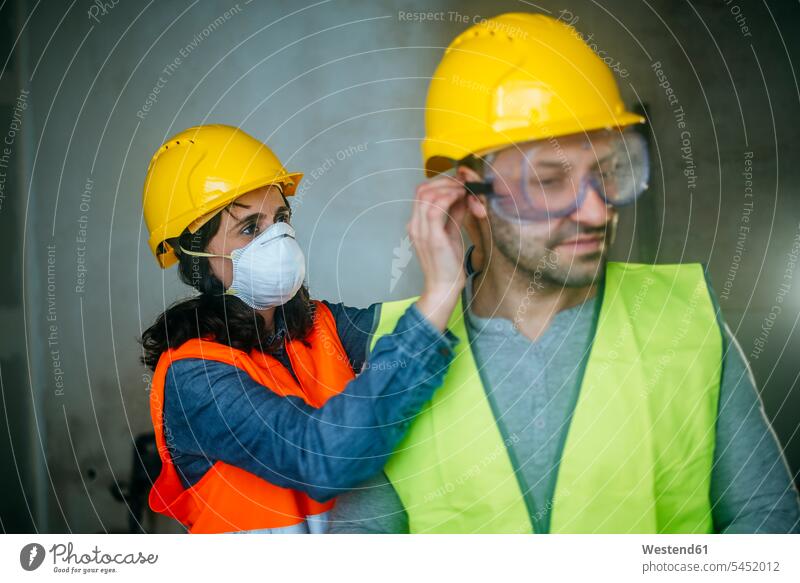 Frau hilft Mann beim Anziehen der Schutzbrille auf einer Baustelle Kollegen Arbeitskollegen arbeiten Bauarbeiter Baustellen Handwerker Handwerksberuf