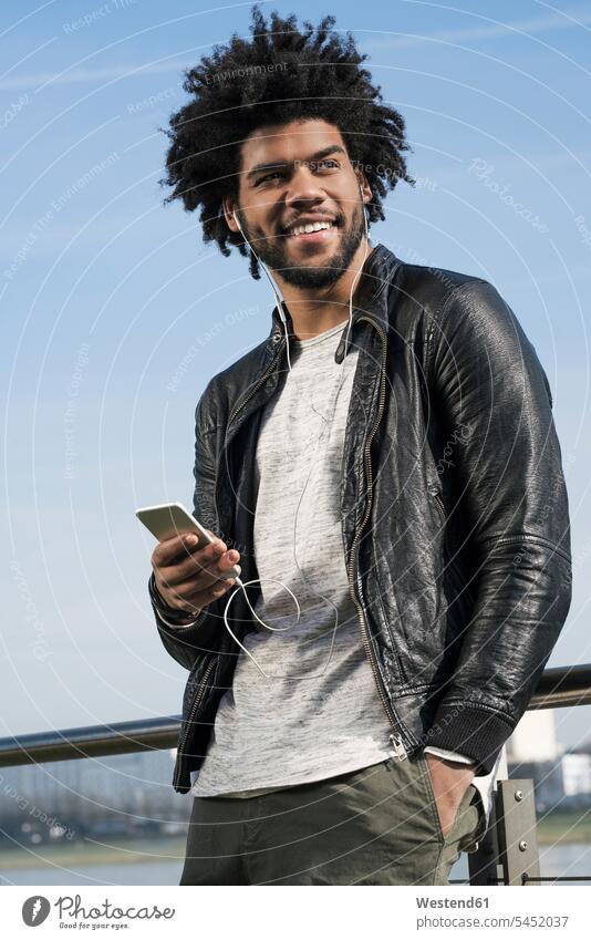 Lächelnder Mann mit Kopfhörern, der auf seinem Smartphone Musik hört lächeln Männer männlich Handy Mobiltelefon Handies Handys Mobiltelefone Erwachsener