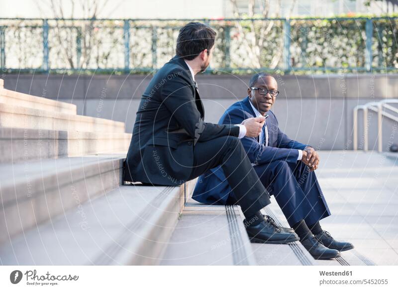 Zwei Geschäftsleute sitzen auf einer Treppe und unterhalten sich Geschäftsmann Businessmann Businessmänner Geschäftsmänner Treppenaufgang Kollegen