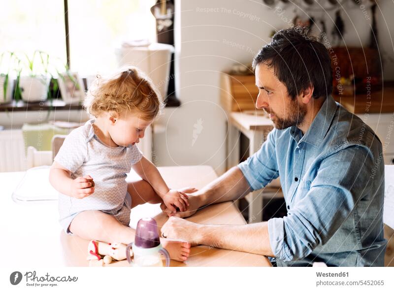 Vater spielt mit kleinem Jungen, der auf dem Küchentisch sitzt Baby Babies Babys Säuglinge Kind Kinder spielen Papas Väter Vati Vatis Papis Walnuss Walnueße