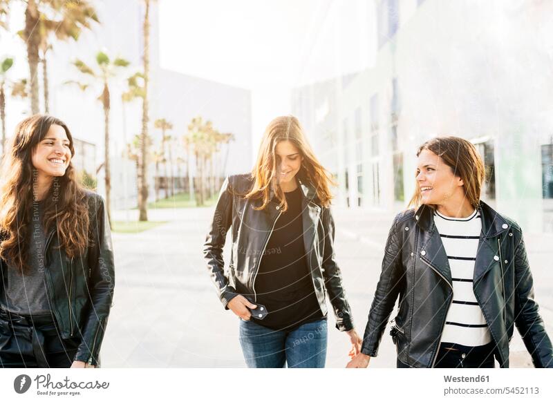 Drei glückliche Freunde in schwarzen Lederjacken Freundinnen Freundschaft Kameradschaft lachen Mode modisch Fashion Frau weiblich Frauen gehen gehend geht