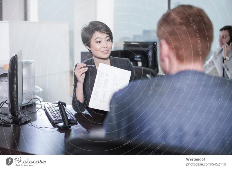 Frau zeigt einem Mann am Schreibtisch im Büro ein Blatt Papier sprechen reden Office Büros Arbeitsplatz Arbeitsstätte Arbeitstelle Business Geschäftsleben