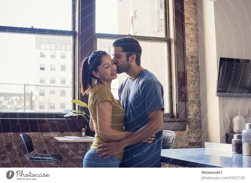 Junges Paar küsst sich in der Küche frisch verliebt sich verlieben liebevoll zaertlich einfühlsam einfuehlsam zärtlich sanft Pärchen Paare Partnerschaft umarmen