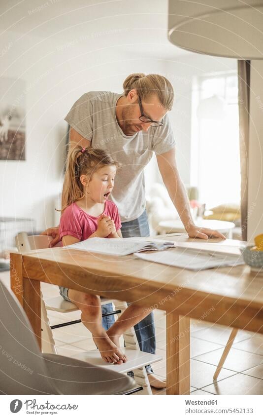 Vater überprüft Hausaufgaben seiner Tochter Kind Familie Mensch Eltern Zuhause Deutschland ein Elternteil prüfender Blick Vaterschaft Mund offen Heft Kindheit