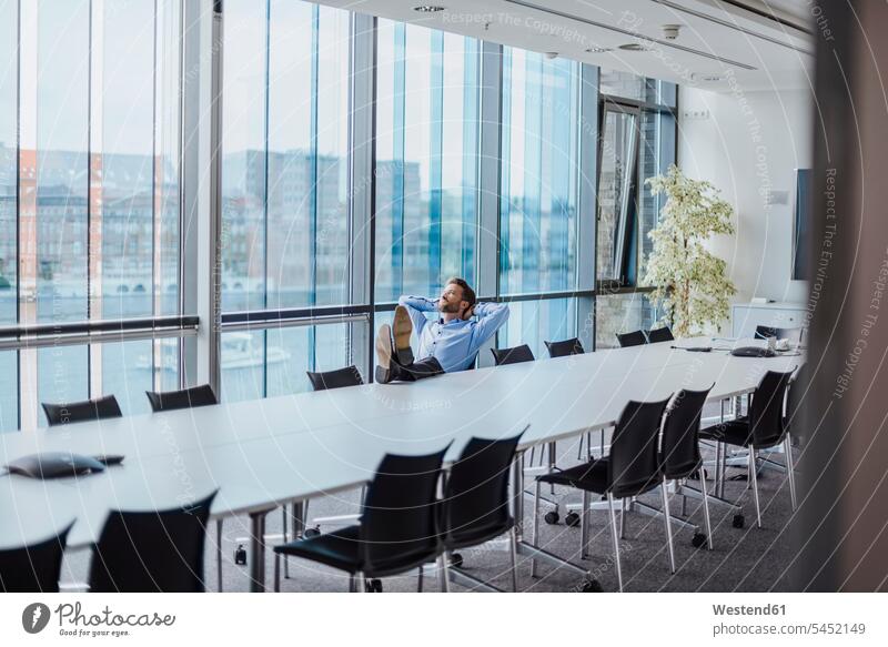 Deutschland, Berlin, Geschäftsmann sitzt im Konferenzraum mit erhobenen Füßen und schaut aus dem Fenster Businessmann Businessmänner Geschäftsmänner