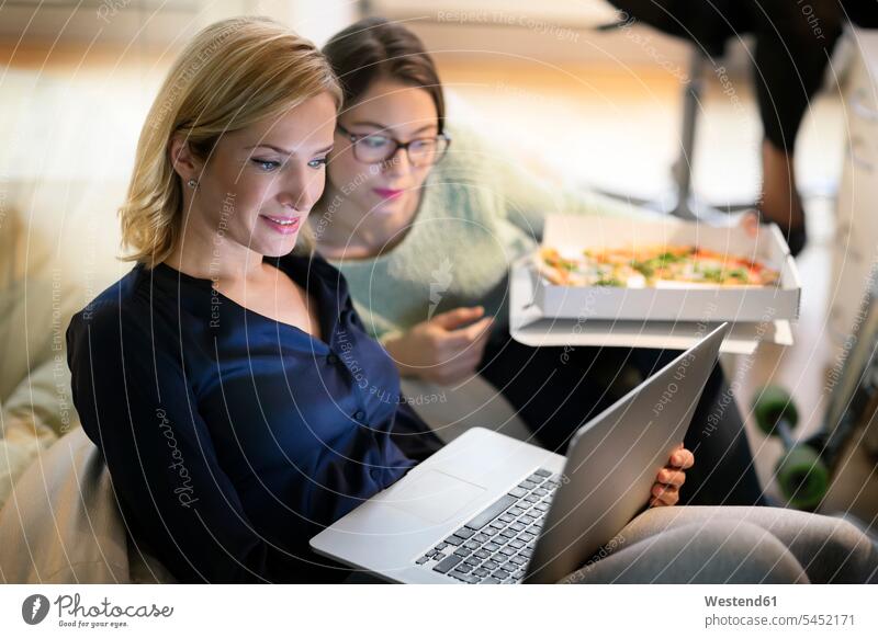 Zwei Businessfrauen im Büro mit Pizza und Laptop Pizzen Geschäftsfrau Geschäftsfrauen Businesswomen Businesswoman Office Büros Kollegin Kolleginnen sitzen
