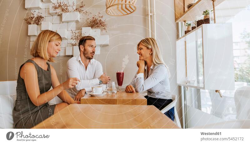 Drei Freunde treffen sich in einem Cafe Kaffeehaus Bistro Cafes Café Cafés Kaffeehäuser sprechen reden lächeln Freundschaft Kameradschaft Gastronomie