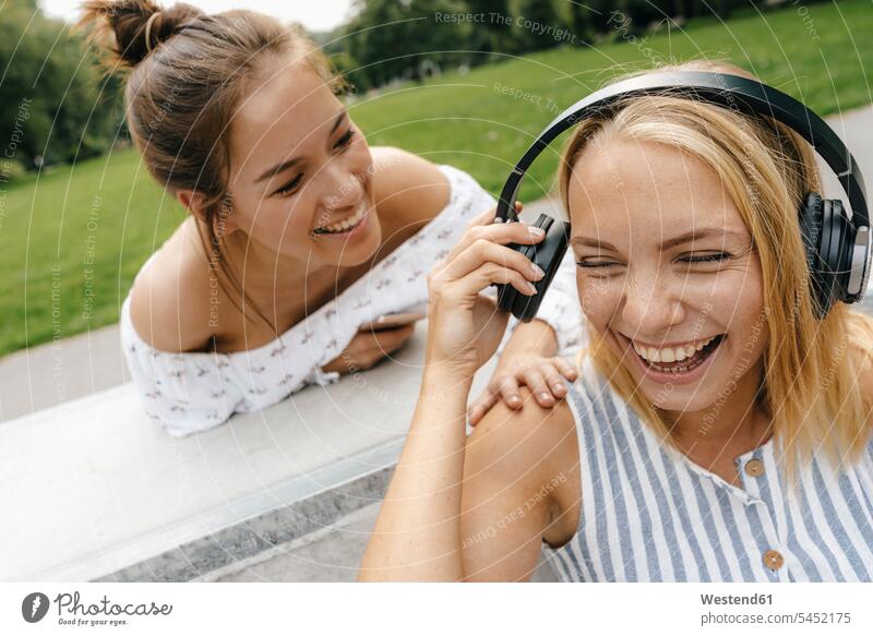 Zwei glückliche junge Frauen mit Kopfhörern im Freien Freundinnen Kopfhoerer Glück glücklich sein glücklichsein weiblich Teilen Sharing Freunde Freundschaft