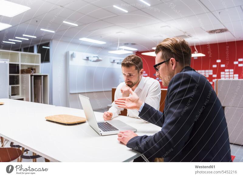 Zwei Geschäftsleute sitzen in einem modernen Büro und diskutieren vor einem Laptop Kollegen Arbeitskollegen Geschäftsmann Businessmann Businessmänner