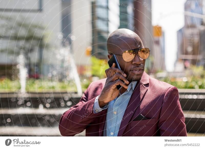 USA, New York City, Manhattan, Porträt eines Geschäftsmannes mit verspiegelter Sonnenbrille am Telefon Smartphone iPhone Smartphones telefonieren anrufen Anruf