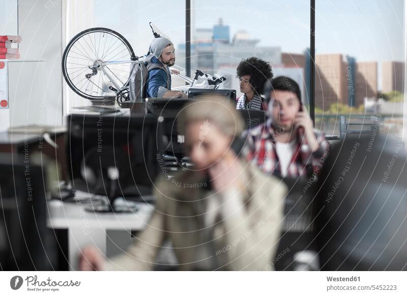Lässiger Mann mit Fahrrad im modernen Büro im Gespräch mit einer Kollegin arbeiten Arbeit Office Büros Bikes Fahrräder Räder Rad Kollegen Arbeitskollegen