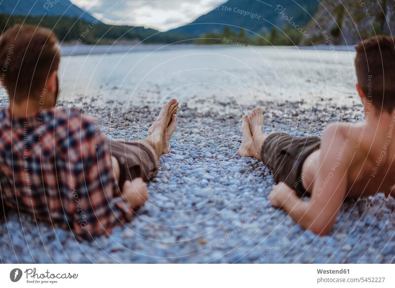 Deutschland, Bayern, Rückansicht von zwei Freunden, die am Flussufer liegen und auf die Ansicht schauen Freundschaft Kameradschaft betrachten betrachtend barfuß