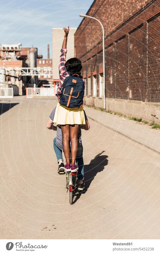 Junges Paar fährt Fahrrad mit einem Mädchen auf einem Gepäckträger stehend jung Pärchen Paare Partnerschaft multikulturell aktiv radfahren fahrradfahren radeln
