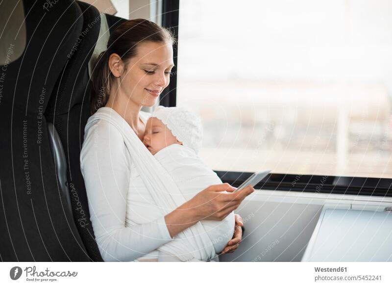 Mutter mit Baby Mädchen reist mit dem Zug und schaut auf Handy lächeln reisen verreisen Mami Mutti Mütter Mama Bahnen Züge Babies Babys Säuglinge Kind Kinder
