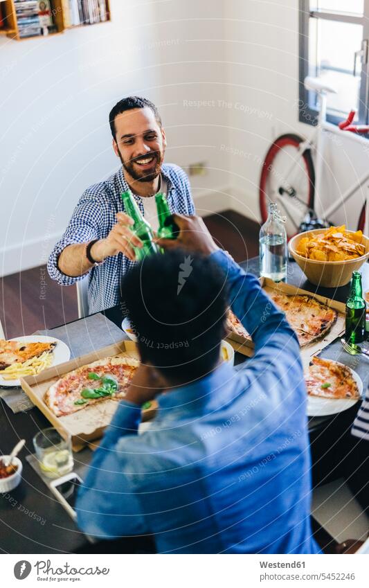 Freunde klirren mit Bierflaschen am Esstisch Pizza Pizzen essen essend anstoßen zuprosten anstossen Tisch Tische Essen Food Food and Drink Lebensmittel