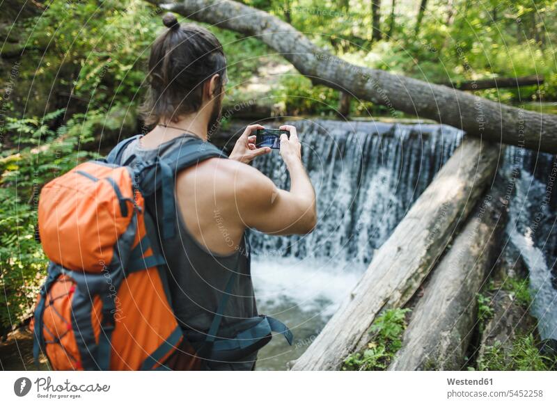 Junger Mann macht ein Handyfoto an einem Wasserfall im Wald Mobiltelefon Handies Handys Mobiltelefone Wanderer wandern Wanderung Männer männlich Telefon