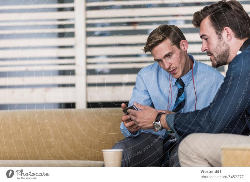 Zwei Kollegen teilen sich ein Mobiltelefon in der Büro-Lounge sprechen reden Arbeitskollegen sitzen sitzend sitzt Office Büros Handy Handies Handys