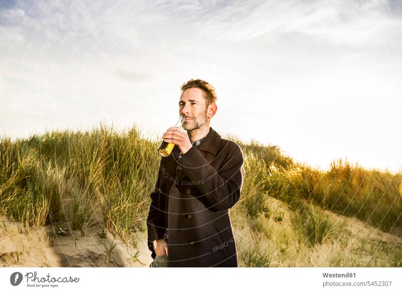 Lächelnde Frau trinkt ein Bier in den Dünen ernst Ernst Ernsthaftigkeit ernsthaft Mann Männer männlich Sanddüne Sanddünen Strand Beach Straende Strände Beaches