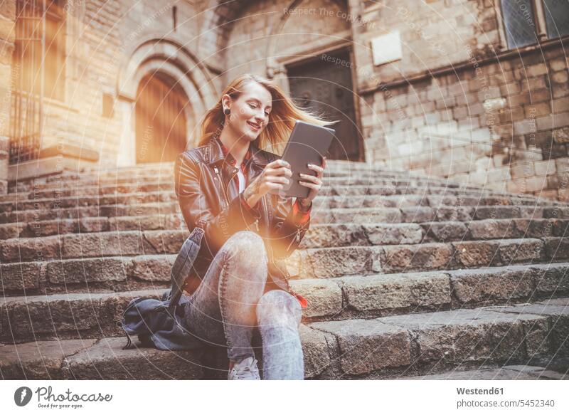 Spanien, Barcelona, lächelnde junge Frau sitzt auf der Treppe und schaut auf das Tablett weiblich Frauen Tablet Computer Tablet-PC Tablet PC iPad