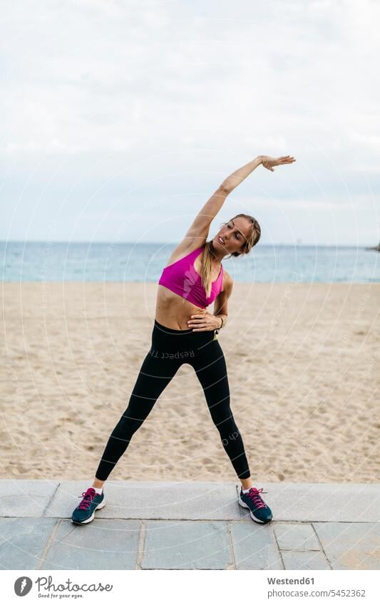 Junge Frau beim Stretching und Aufwärmen für das Training am Strand Beach Straende Strände Beaches weiblich Frauen dehnen strecken trainieren aufwärmen