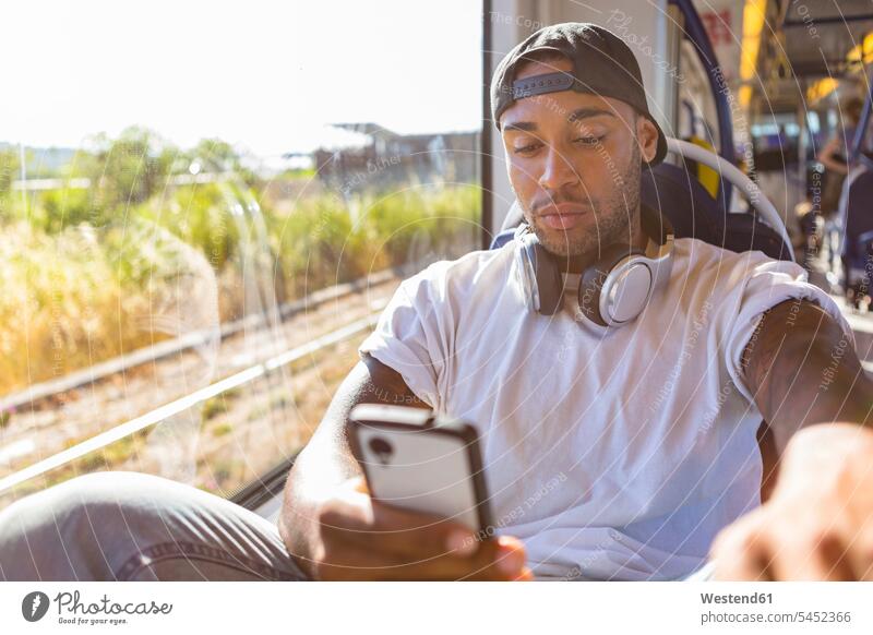 Porträt eines jungen Mannes in der Straßenbahn, der auf ein Smartphone schaut iPhone Smartphones Trambahn S-Bahn S-Bahnen Strassenbahnen Straßenbahnen Männer